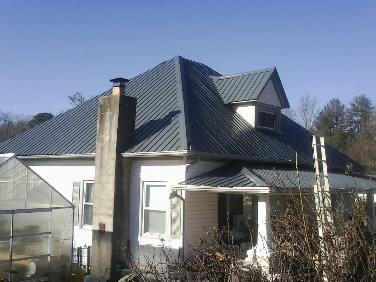 Dark blue standing seam metal roof on a white farmhouse with dormer — Slate & Tile Roof Repair by Roofing Brothers in Garysburg