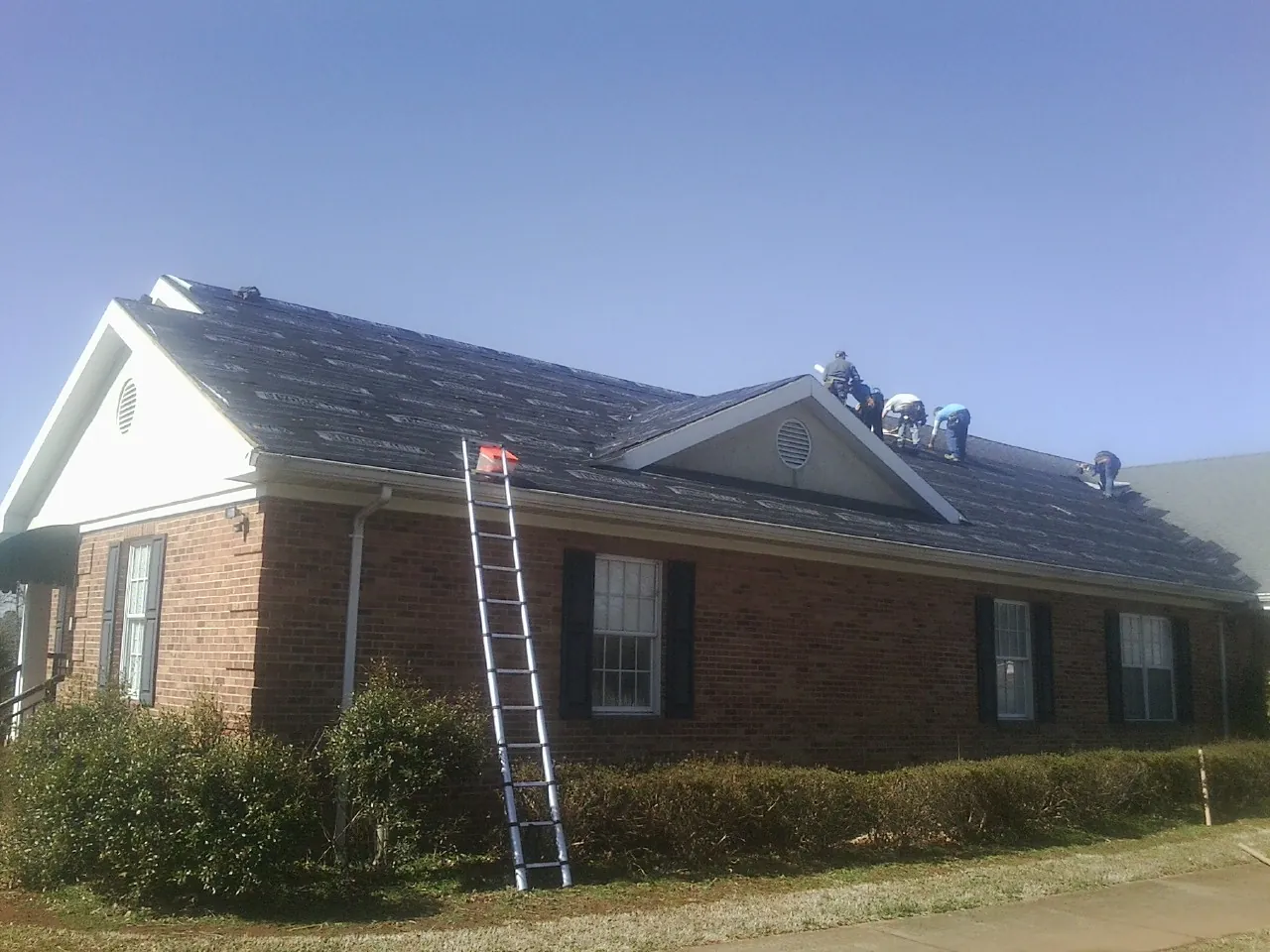 Crew tearing shingles off a brick ranch roof with a ladder set — Metal Roof Repair work by our crew in Garysburg