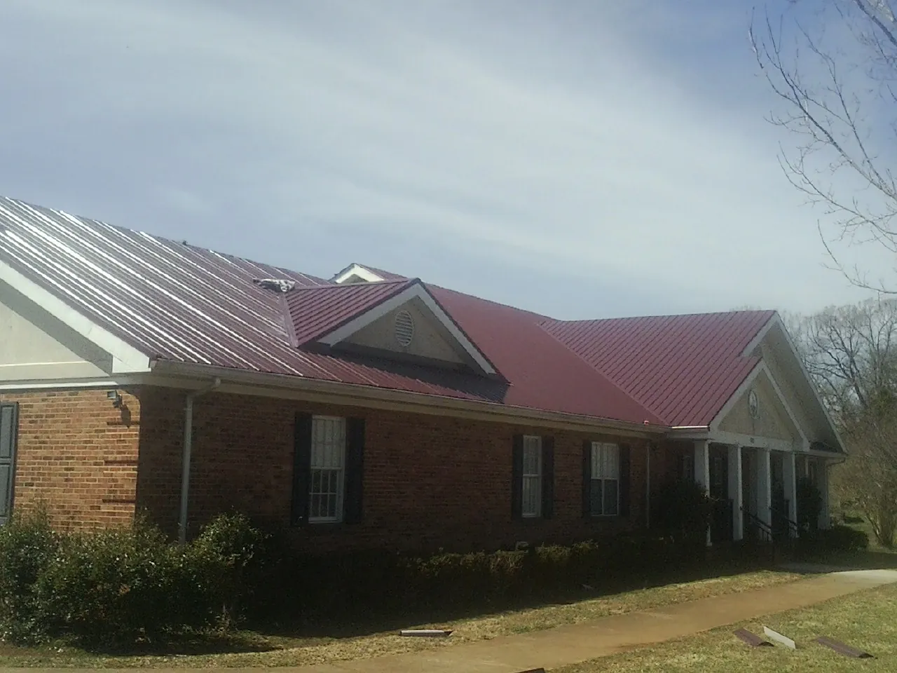 Red metal roof with gabled entries on a long brick building, from a Hail Damage Roof Repair job in Garysburg