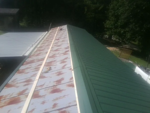 Old rusted panels beside newly installed green metal roofing — Wind Damage Roof Repair by Roofing Brothers in Garysburg