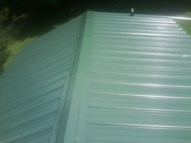 New green metal panels meeting at the ridge of a roof — Flat Roof Repair work by our crew in Garysburg