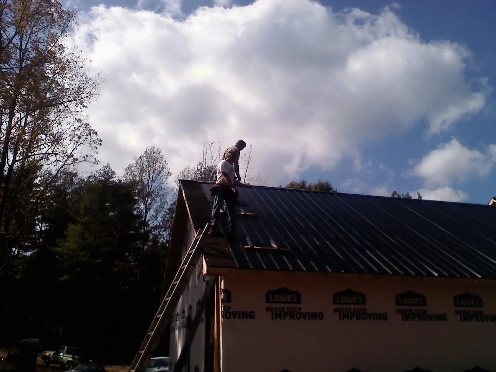 Roofer fastening dark metal panels high against a cloudy sky, from a Roof Inspection job in Garysburg