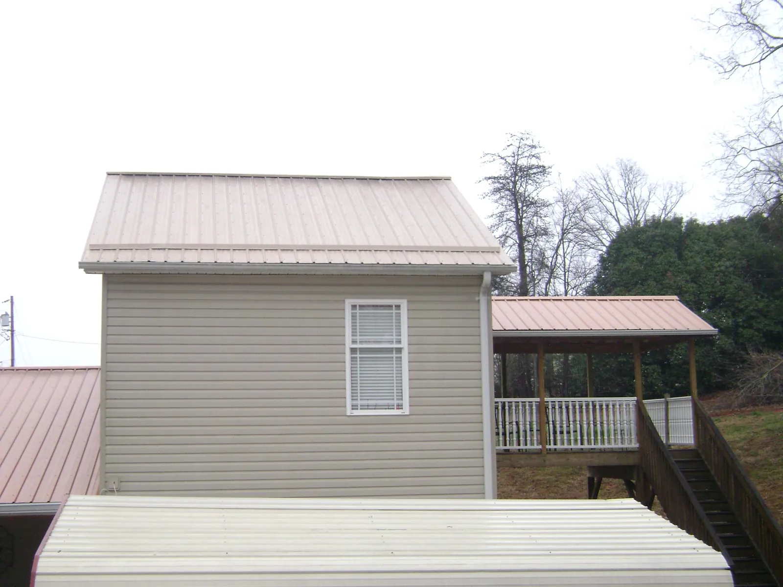 Tan metal roofs on a two story addition and attached porch, from a Roof Replacement job in Garysburg